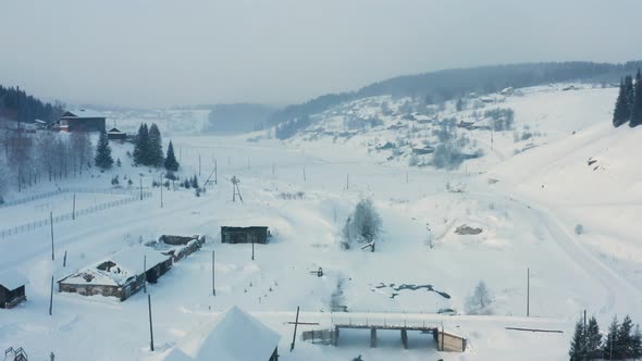Aerial View of a Village in the Snow on the Bank of a Frozen River alt