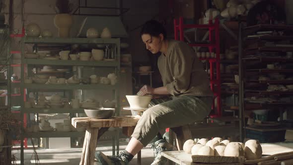 Craftswoman Is Sitting On Potter's Wheel and Making Bowl alt