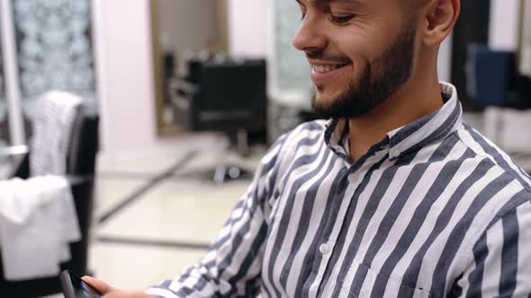 Charismatic Young Man Checks the News on the Phone, Happily, While the Miller Dries His Hair alt