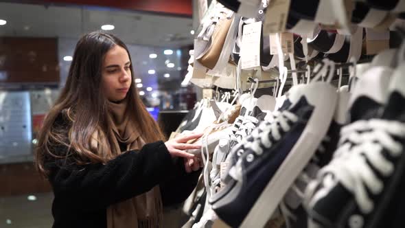 A Young Woman in a Shoe Store Chooses Sneakers
