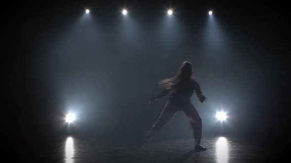 Woman with Long Hair Practicing Capoeira in Darkness Against Spotlight in Studio alt