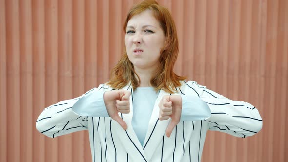 Slow Motion Portrait of Disgusted Redhead Lady Showing Thumbsdown Hand Gesture and Wrinkling Nose alt