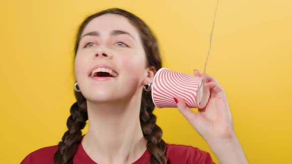 A smiling woman communicates on a toy walkie-talkie made out of a paper cup. alt