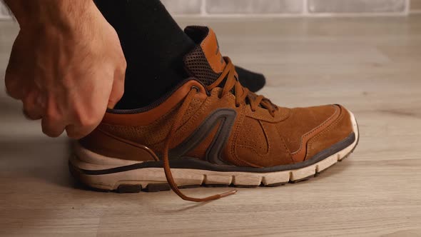 A Closeup of a Man's Black Socked Foot Putting on a Brown Leather Walking Sneaker alt