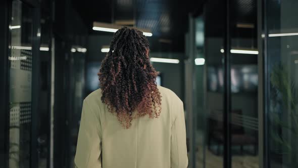 The Camera Follows the Back of a Business Black Woman Down the Corridor alt