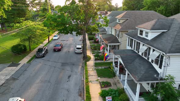 Establishing shot of cars driving on small town street. Pride flags and American flags visible hangi alt