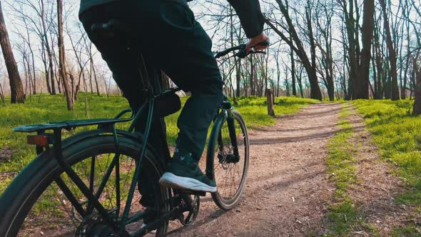Young Guy Rides a Bicycle Along a Path in a Green Forest Rear View in Slow Mo alt
