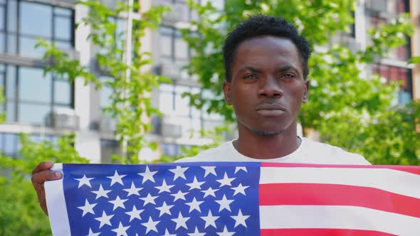 Close Up Afroamerican Man Holding an American Flag and Looks Camera alt