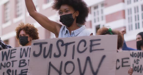 Diverse group of men and women holding placards shouting raising fists during protest wearing masks alt