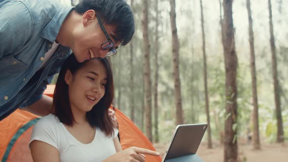 Young asia campers couple using tablet in chairs by tent in forest.