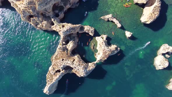 Drone shot of kayaks and boats passing in the ocean, people exploring caves and tunnels. alt