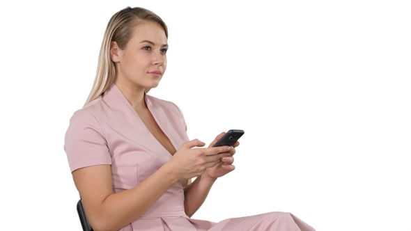 Smiling Blonde Woman Sitting and Using Smartphone on White alt