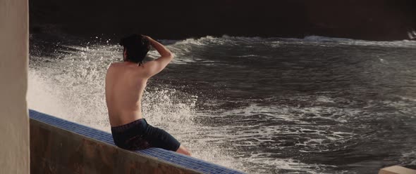 Young man topless taking a photo seated on a balcony by the sea alt