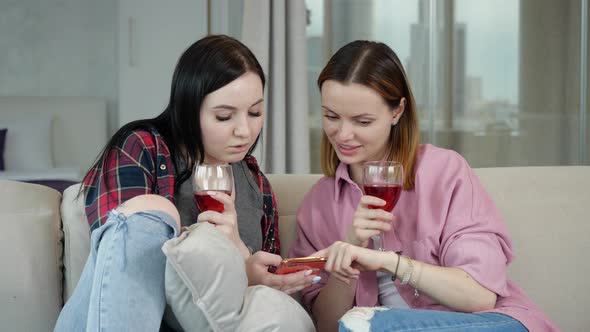 Two Young Girls Talking Drinking Wine and Watching Messages on Their Phone