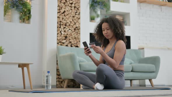 African Woman Making Online Payment on Smartphone on Yoga Mat alt