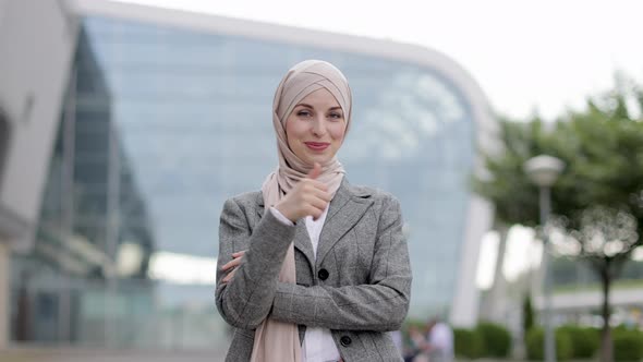 Muslim Woman in Hijab Posing Outside in Front of Modern Building and Showing Thumb Up alt