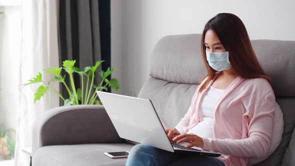Young woman wearing medical mask sitting at living room and working