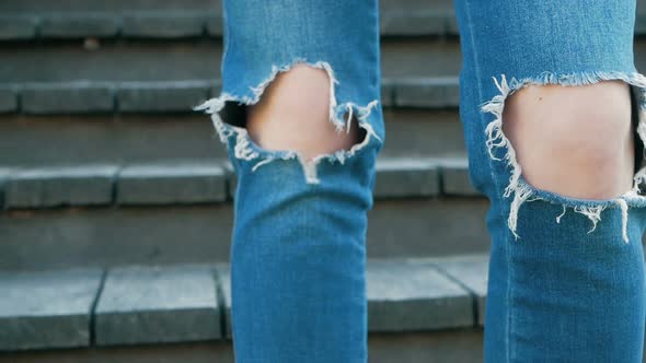 Knees of a girl in torn blue jeans. Teenager and fashion. Clothes for young people. Stylish denim pa