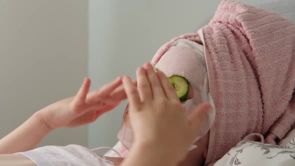 Cute Little Girl in a Towel Lying with Cucumbers on Her Face Spa at Home