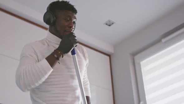 Happy Young Handsom Black Man Cleaning the Flor While Listening the Music and Dancing alt