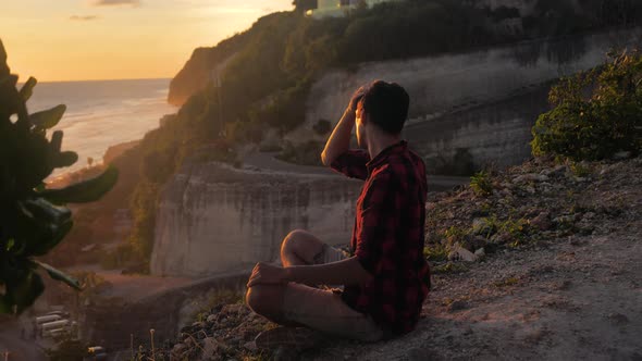 Man Meditates While Sitting on a Rock Against a Beautiful Sunset