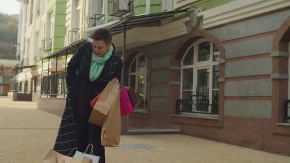 Mature Woman Getting Phone Out of Pocket Letting Fall Bags Outdoors alt