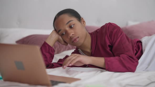 Bored Young African American Woman Putting Head on Bed Closing Eyes Working Online From Home Office alt