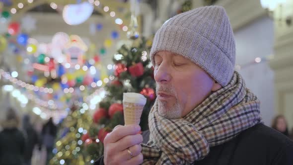 An Elderly Bearded Man Eats Milk Ice Cream in a Waffle Cone at a Christmas Market in a Store