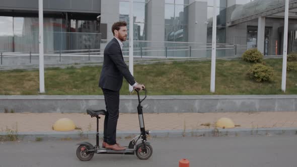 Young Modern Business Man in a Suit Riding an Electric Scooter alt