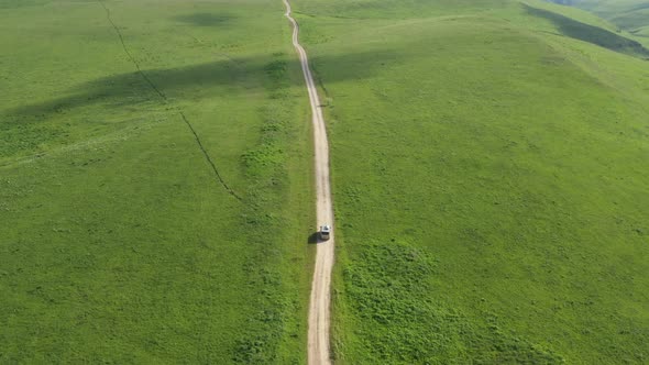 Top view on the driving car of the mountain road through the green field