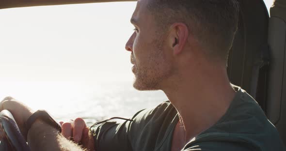 Happy caucasian man sitting in car enjoying the view on sunny day by the sea alt