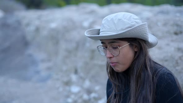 Close Side View of Young Woman in Hat and Glasses Eating in Nature alt
