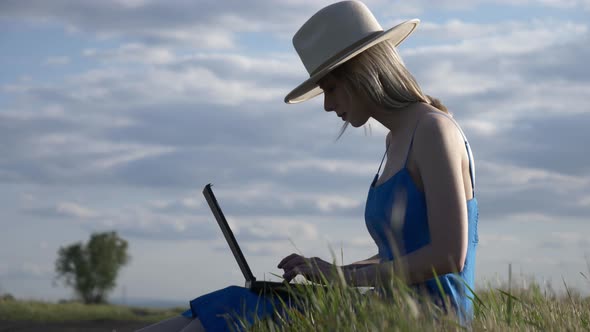 Girl in blue dress with laptop computer sit on country road in summer.