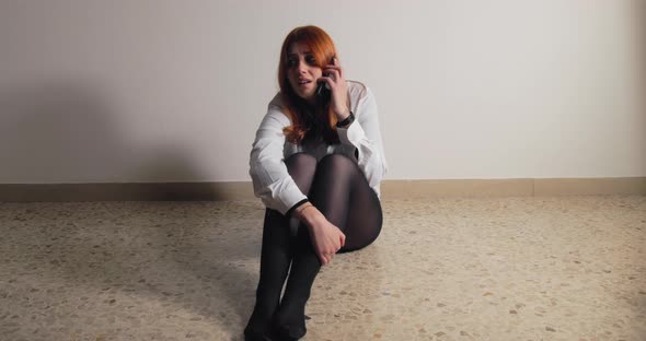 Girl Sitting on the Ground Talking on the Phone Scared of the Abuser in House alt