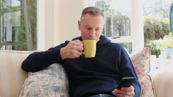 Man using mobile phone while having coffee in living room  alt