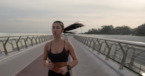 Fit Female in Sportswear Running on Modern Bridge During Fitness Training in Evening in City alt