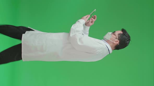 Side View Of Asian Doctor With Stethoscope Wearing Mask, Using Tablet While Walking On Green Screen alt