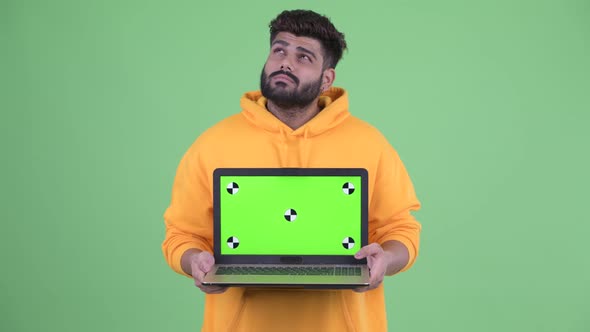Happy Young Overweight Bearded Indian Man Thinking While Showing Laptop alt