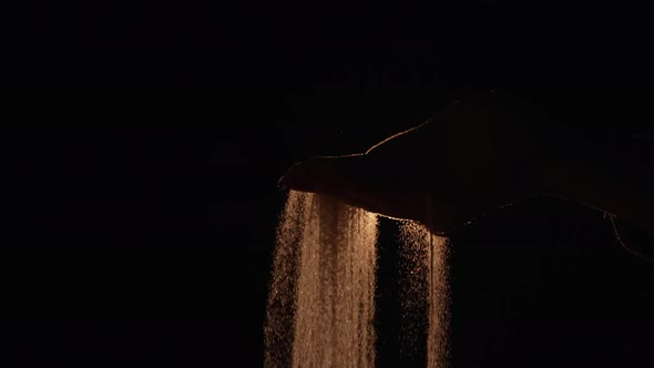 The Dark Silhouette of a Female Hand Spilling Sand From the Palm of Her Hand on a Black Background alt