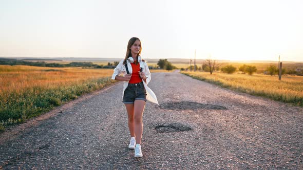 Young Happy Teenage Girl Walks Across Field Wearing Headphones and Sings Song alt