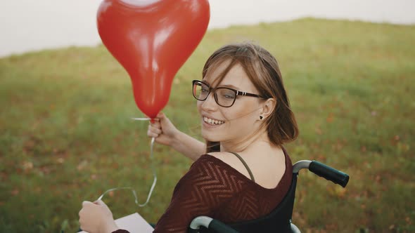 Disabled Caucasian Young Woman with Red Balloon Looking Over the Shoulder and Smiling  alt