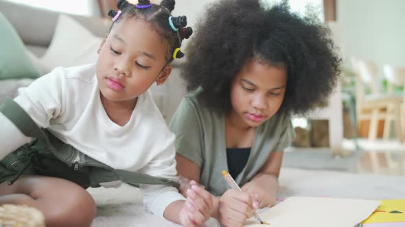 4K Little African girl sibling using color pencil drawing and painting on paper book together.
