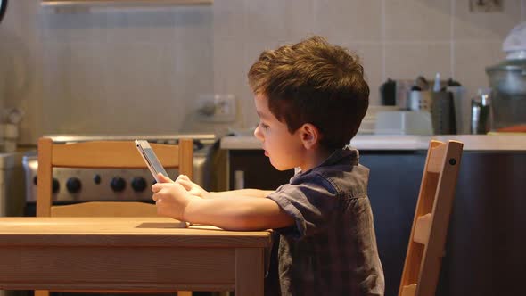 Cute Little Child Uses A Tablet Pc At A Table At Home. Casual Clothes