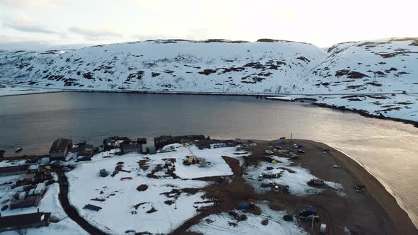 The Drone Flies Over a Small Northern Village on the Coast Surrounded By Snowcovered Cliffs