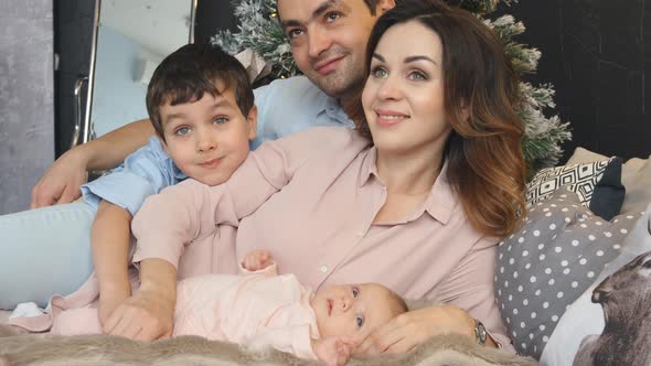Young family with son and newborn lie on a bed in Christmas