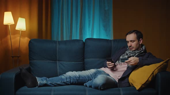 Man Lies on a Cozy Sofa and Makes Payment Online By Credit Card alt