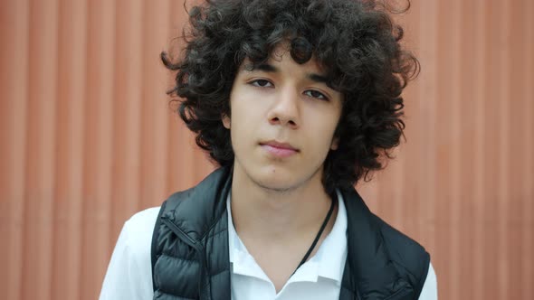 Portrait of Curlyhaired Teenager Looking at Camera with Serious Face Standing Outdoors Alone alt