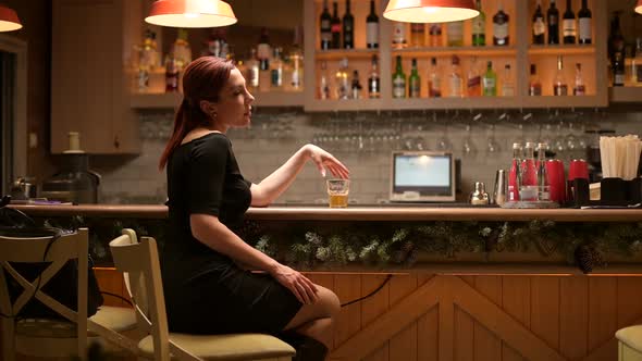 Lonely young woman sits in an empty bar in the evening and drinks alt
