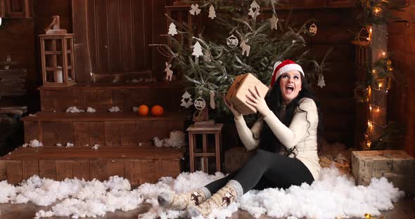 Woman in Santa Hat with Gift Sitting By the Christmas Tree