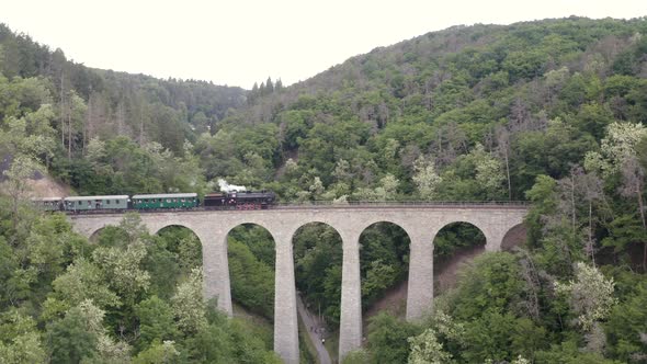 Steam train passing over a stone viaduct in a mountain valley,zooming. alt